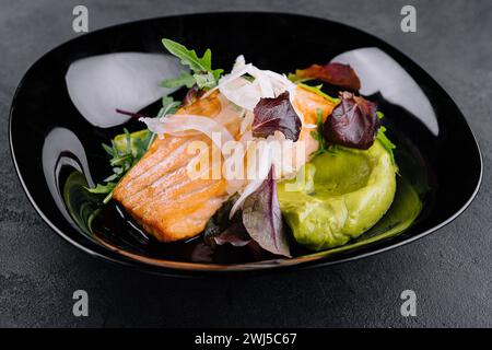 Primo piano di filetto di salmone grigliato con germogli di rucola verde con purè di avocado su un piatto. Foto Stock