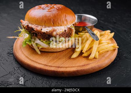 Delizioso hamburger con salsa al formaggio e patatine fritte su un tavolo di legno Foto Stock