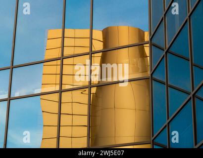 Riflesso distorto di un edificio giallo nelle finestre a specchio di un edificio per uffici Foto Stock