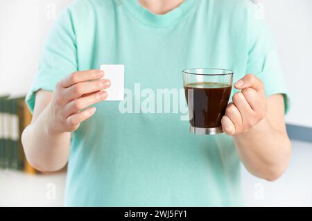 Colpo ritagliato di una donna che tiene le mani una tazza di caffè e saccarina a casa Foto Stock