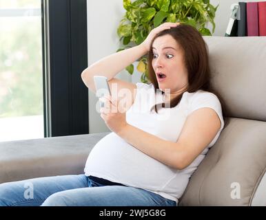 Foto di una donna incinta stupita con promozione online a casa Foto Stock