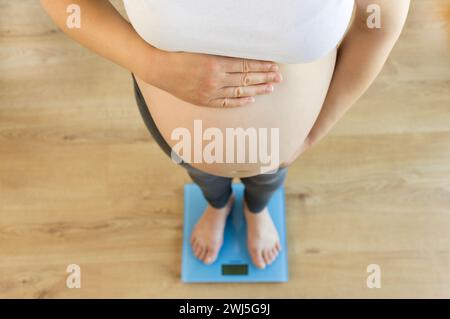 Ripresa ritagliata ad angolo alto di una donna incinta che si pesa su una bilancia a casa Foto Stock