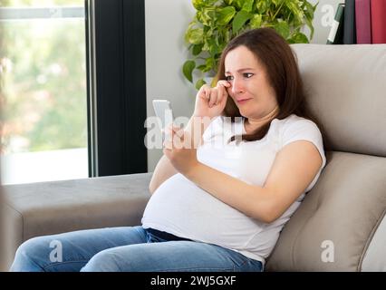 Triste adolescente che piange dopo aver letto un messaggio telefonico a casa Foto Stock