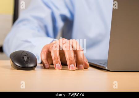 Primo piano di una mano caucasica che le tocca con ansia la scrivania mentre lavora su un laptop in ufficio. Concetto di ansia, stress, b Foto Stock