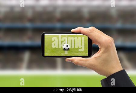 uomo d'affari che fotografa un pallone da calcio con il telefono in uno stadio Foto Stock