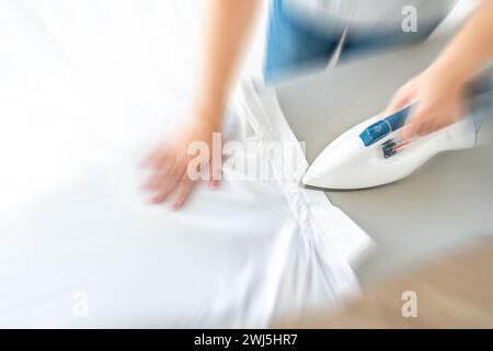 Donna mani che stira il colletto bianco della camicia sull'asse da stiro, vista dall'alto con effetto di sfocatura del movimento Foto Stock