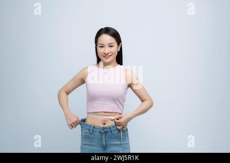 donna in jeans grandi vecchi che misura la vita con del nastro, mostrando i risultati di una dieta dimagrante Foto Stock