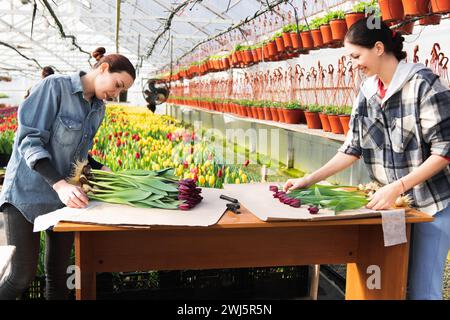 Una donna avvolge un mazzo di fiori in carta artigianale. Bouquet di tulipani viola. Vendita di bouquet dalla serra. Foto Stock