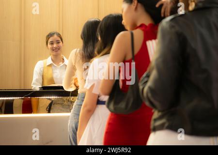 Giovane donna asiatica in fila per acquistare biglietti per il cinema e in mano popcorn e bevande, sorridente venditore di biglietti che serve. Foto Stock