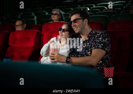 In un cinema, Una coppia giovane che indossa occhiali 3D guarda film e mangia popcorn. Foto Stock