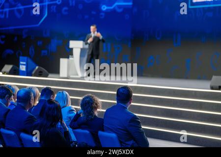 Immagine sfocata di un relatore aziendale su un podio che coinvolge un pubblico attento in una moderna sala conferenze. Foto Stock