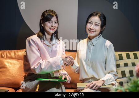 Le due donne d'affari asiatiche sedute insieme su un divano. Foto Stock