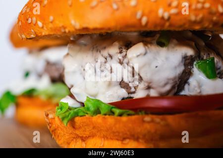 Primo piano due succosi hamburger con salsa di formaggio blu con bunsa di sesamo, verdure fresche e sottaceti su un tavolo di legno Foto Stock