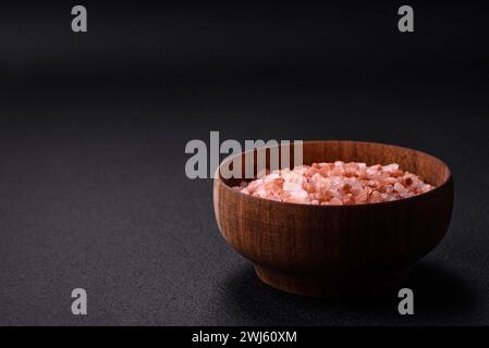 Sale himalaya rosa in una ciotola di legno su fondo di cemento scuro. Condimenti e additivi in cucina Foto Stock