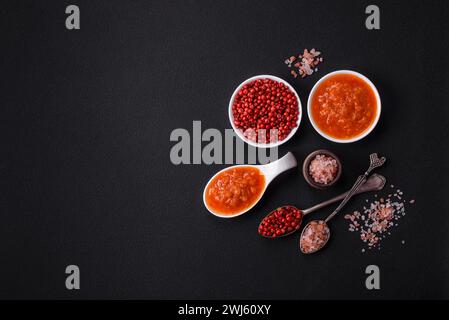 Salsa di adjika rossa o ketchup con spezie ed erbe su fondo di cemento scuro Foto Stock