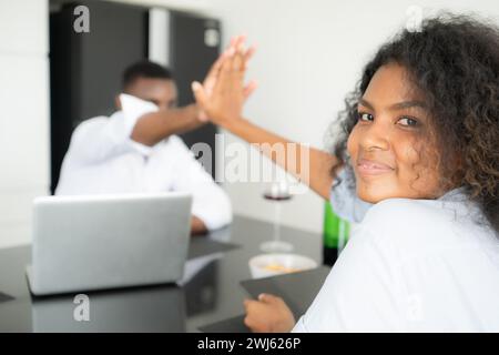 Entrambe le giovani aziende bevono vino e utilizzano i loro computer portatili per condividere informazioni nel loro salotto di casa. Foto Stock