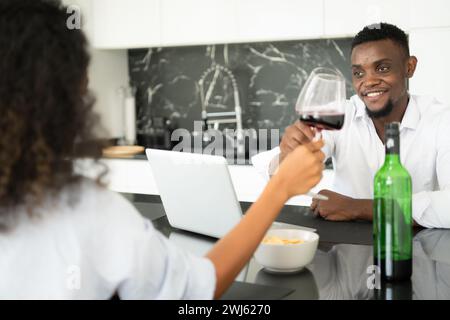 Entrambe le giovani aziende bevono vino e utilizzano i loro computer portatili per condividere informazioni nel loro salotto di casa. Foto Stock