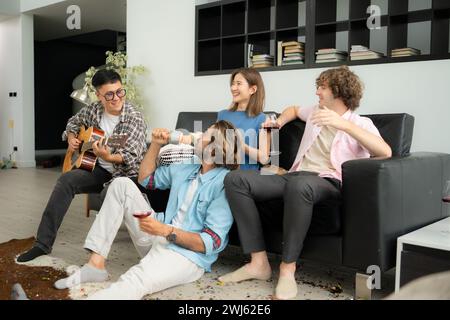 Gruppo multietnico di amici che si divertono a suonare la chitarra e a cantare insieme a casa Foto Stock