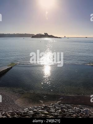 La piscina del mare di Devil’s Point a Plymouth. L'acqua di mare entra sopra il muro della piscina con una marea di primavera strisciante nel febbraio 2024. Firestone Bay e Drakes Island Foto Stock