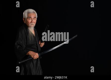 Samurai giapponese senior con spada katana su sfondo nero, foto in studio Foto Stock