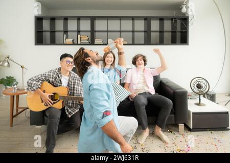 Gruppo multietnico di amici che si divertono a suonare la chitarra e a cantare insieme a casa Foto Stock