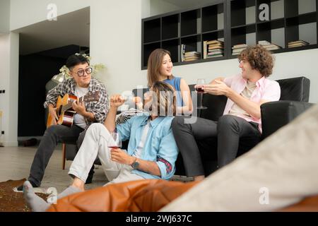 Gruppo multietnico di amici che si divertono a suonare la chitarra e a cantare insieme a casa Foto Stock