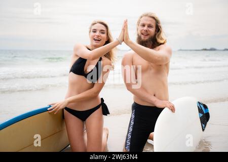 Due surfisti che danno cinque in alto sulla spiaggia. Due surfisti che si divertono sulla spiaggia. Foto Stock