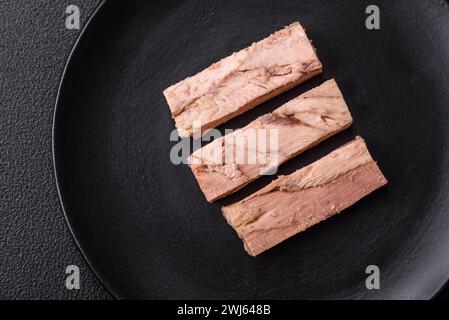 Deliziosa carne di tonno in scatola con sale, spezie e olio su fondo di cemento scuro Foto Stock