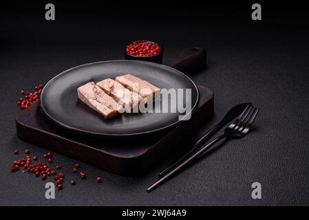 Deliziosa carne di tonno in scatola con sale, spezie e olio su fondo di cemento scuro Foto Stock