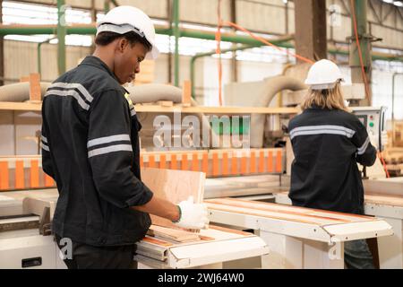 Entrambi i lavoratori lavorano in una fabbrica di lavorazione del legno, lavorando con segatrici e tagliatrici del legno per produrre fogli di legno per la produzione di pa Foto Stock