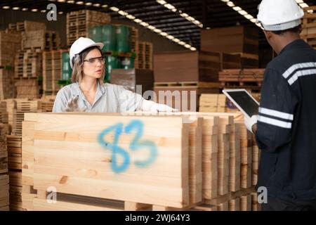 Giovani operai di magazzino di sesso maschile e femminile che utilizzano tablet digitali per lavorare in una fabbrica di legno, controllando la correttezza delle tavole Foto Stock