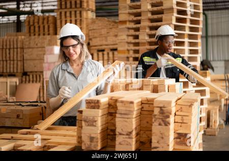 Giovani operai di magazzino di sesso maschile e femminile che utilizzano tablet digitali per lavorare in una fabbrica di legno, controllando la correttezza delle tavole Foto Stock