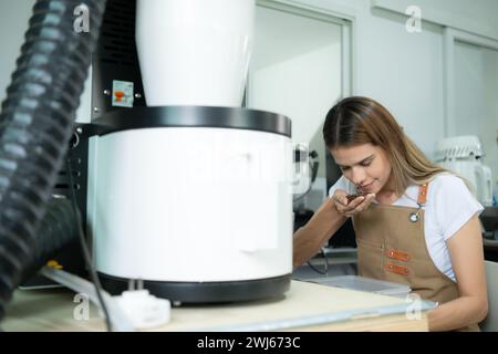 Giovane donna in grembiule che utilizza un tablet digitale per controllare la qualità dei chicchi di caffè con torrefazione digitale Foto Stock
