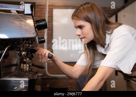 Giovane barista che prepara il caffè in caffetteria. Barista donna che utilizza una macchina per il caffè. Foto Stock