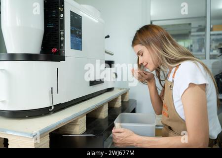 Giovane donna in grembiule che utilizza un tablet digitale per controllare la qualità dei chicchi di caffè con torrefazione digitale Foto Stock