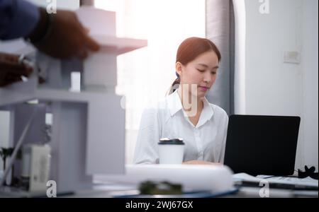 Ritratto di una giovane donna architetto seduta alla sua scrivania in ufficio con un computer portatile Foto Stock