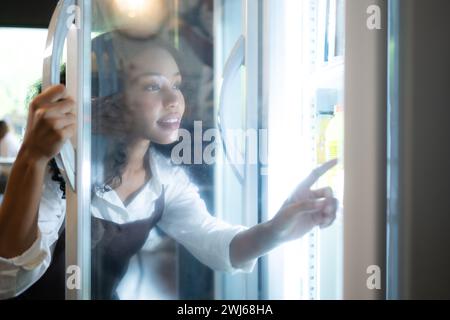 Il proprietario di un bar guarda all'interno del frigorifero per recuperare cibo fresco e servire un cliente. Foto Stock