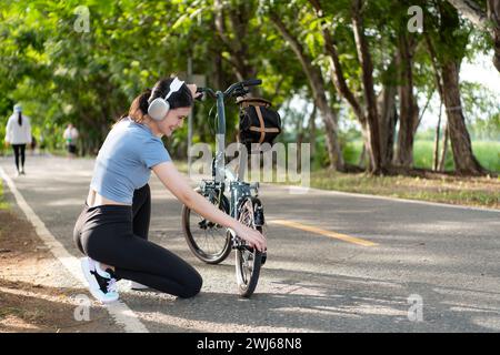 Una giovane donna ascolta la musica con le cuffie mentre controlla la disponibilità della sua bicicletta. prima di guidare su una pista ciclabile nel Foto Stock