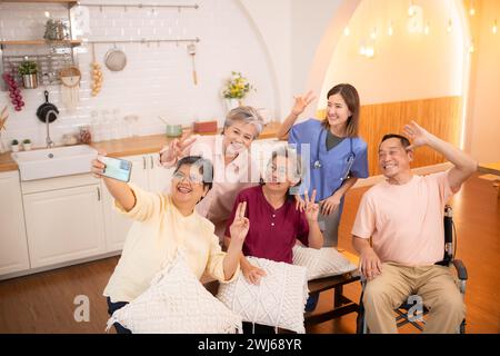 Gruppo di asiatiche senior e caregiver che si divertono con i selfie nella casa di cura. Foto Stock