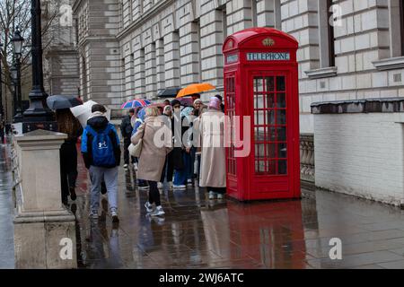 Londra, Regno Unito, 13 febbraio 2024 fila turistica sotto la pioggia con ombrelloni per scattare foto dell'iconica cabina telefonica rossa di Londra e godersi i siti di Londra nonostante la pioggia credito: Richard Lincoln/Alamy Live News Foto Stock