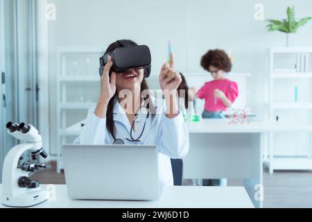 Scienziata femminile che utilizza il visore per la realtà virtuale mentre colleghi lavorano in background in laboratorio Foto Stock