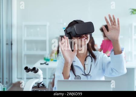 Scienziata femminile che utilizza il visore per la realtà virtuale mentre colleghi lavorano in background in laboratorio Foto Stock