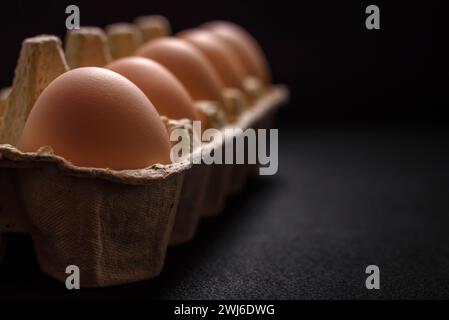 Uova fresche di pollo crude di colore beige in un vassoio di cartone su fondo di cemento scuro Foto Stock