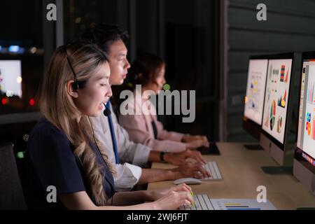 Gruppo di intermediari di borsa internazionali che indossano cuffie e auricolari che lavorano attivamente durante la notte in ufficio, concetto di età dell'assistenza clienti Foto Stock