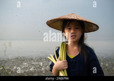 Una bambina assiste la sorella maggiore nella raccolta dei fiori di loto. Concetto di abitazione rurale in Thailandia Foto Stock