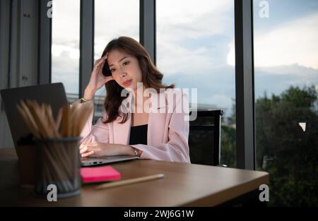 Ritratto di una giovane donna d'affari asiatica che lavora straordinari su un laptop la sera in ufficio Foto Stock