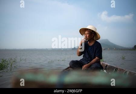 Un pescatore si rilassa su una barca sul lago mentre fuma. Foto Stock