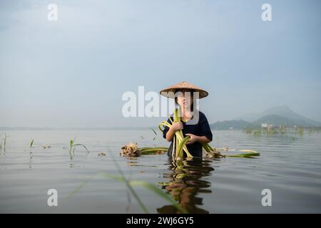 Una bambina assiste la sorella maggiore nella raccolta dei fiori di loto. Concetto di abitazione rurale in Thailandia Foto Stock