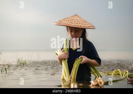 Una bambina assiste la sorella maggiore nella raccolta dei fiori di loto. Concetto di abitazione rurale in Thailandia Foto Stock