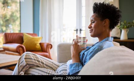 Una donna matura a casa beve un caffè rilassante sul divano nella sala Foto Stock